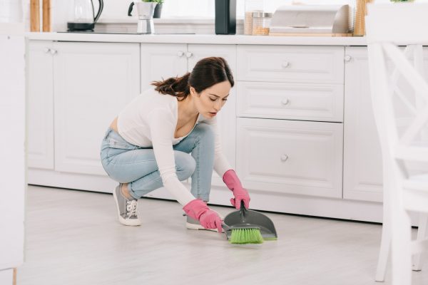 attractive, young housewife sweeping floor with brush and scoop